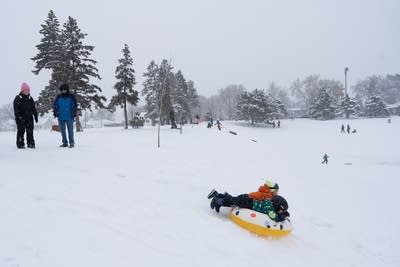 Two kids slide down a snow hill