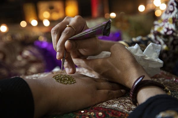 Hajira Begum draws a mandala henna design on Fatma Sheekh's hand.