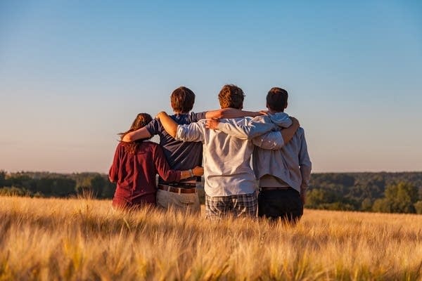 A group of friends stand with arms around one another in an open field.