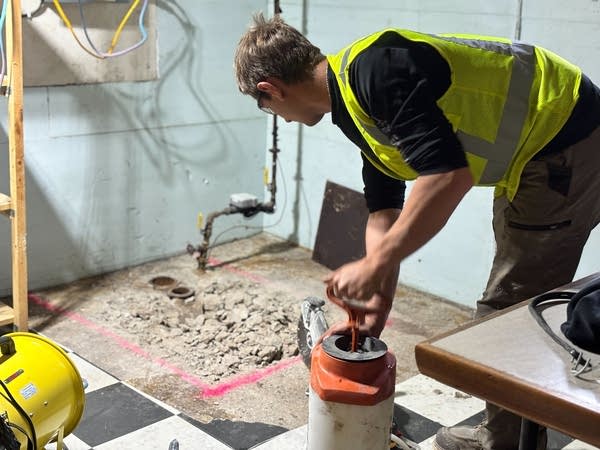 A construction worker prepares a saw to use on a basement floor.
