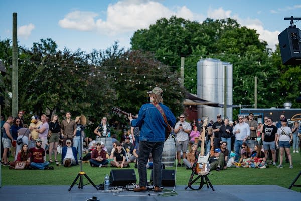 A musician sings and plays guitar on an outdoor stage
