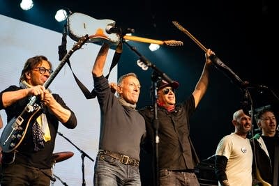 Bruce Springsteen and Tom Morello hold up their guitars.