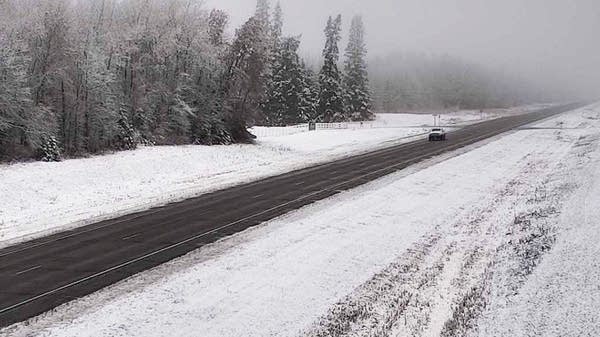 A vehicle travels along a highway in snowy weather