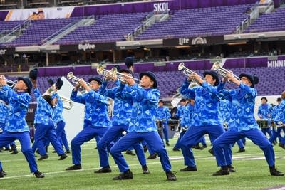 A marching band performs on the field of a football stadium.