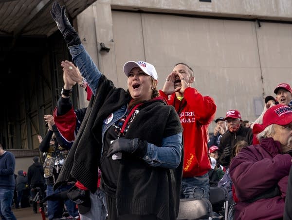 People cheer nearby a large hangar building.