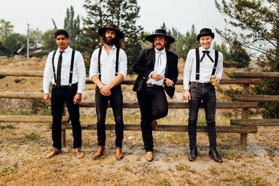 Four men in button-down shirts standing by a rail fence in a rural area