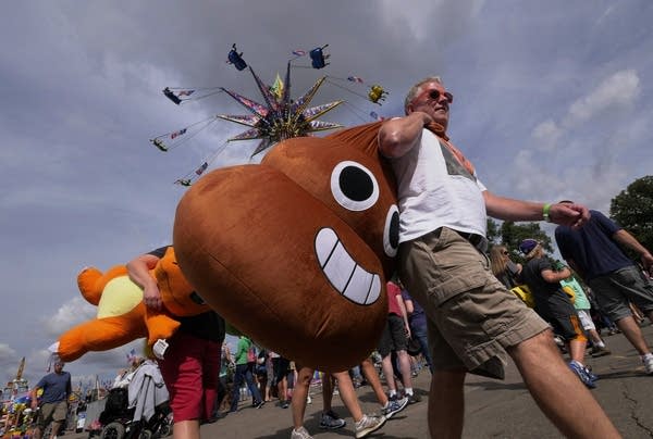 Chip Cramer of Big Fork, Minn., and his family carry the prizes they won on the Midway at the Minnesota State Fair Friday August 26, 2016. Of his giant smiling poo emoji, Chip commented, "They do say I'm full of it."