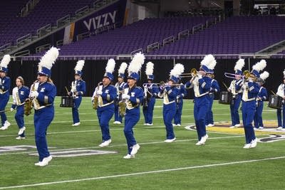 A marching band performs on the field of a football stadium.