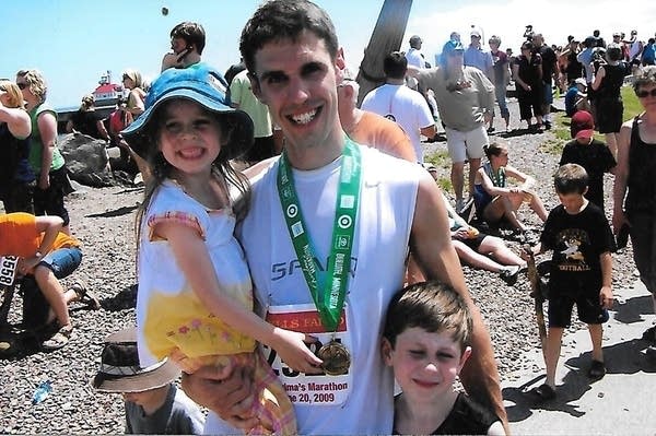 A man poses for a photo with two children wearing a medal after a race.