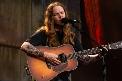 A musician sings and plays flatpick guitar on a large outdoor stage