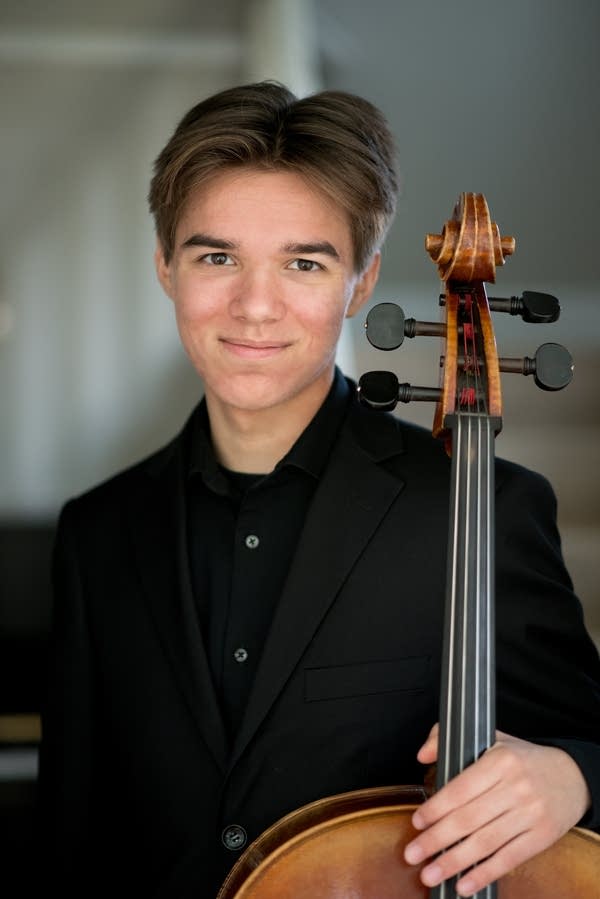 A young man poses with a cello for a portrait