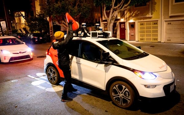 A member of SafeStreetRebel, a group of anonymous anti-car activists, places a cone on a self-driving robotaxi to disable it in San Francisco, California on July 11, 2023. Members of SafeStreetRebel, a group of anonymous anti-car activists, have been actively calling for participants to help protest the spread of robotaxis for malfunctioning and blocking traffic.