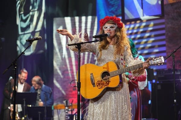 A woman in a sparkly dress and cat-eye glasses performs onstage
