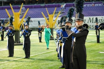A marching band performs on the field of a football stadium.