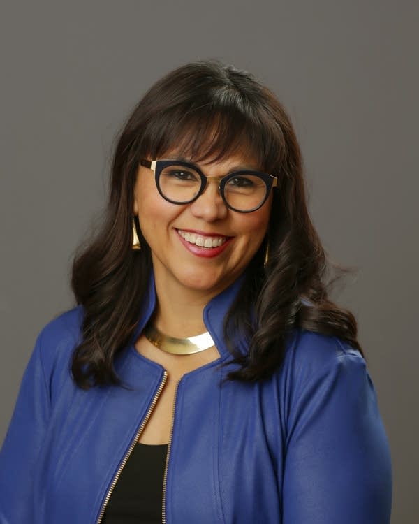 headshot of woman wearing a blue jacket, silver necklace and glasses