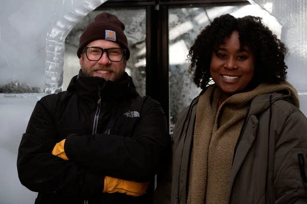 Two people stand in a structure made of ice blocks.