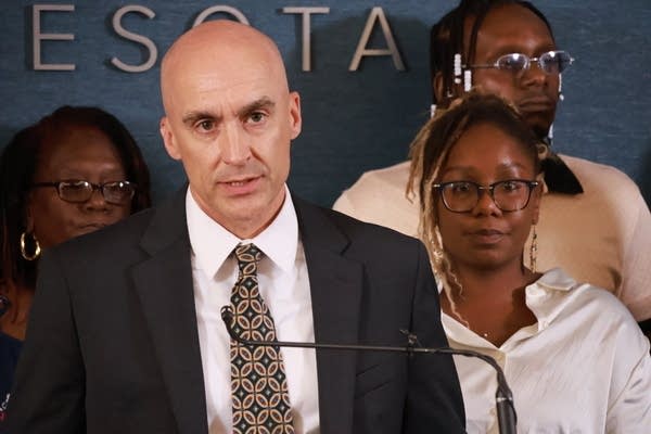 man in black suit speaks at microphone