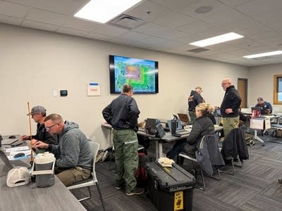 A team works on laptops while a map of a wildfire is shown on a mounted TV.