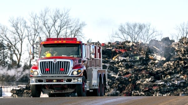 A truck drives past a pile of cars. 