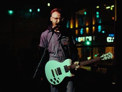 A perfson sings into a microphone while holding a guitar.