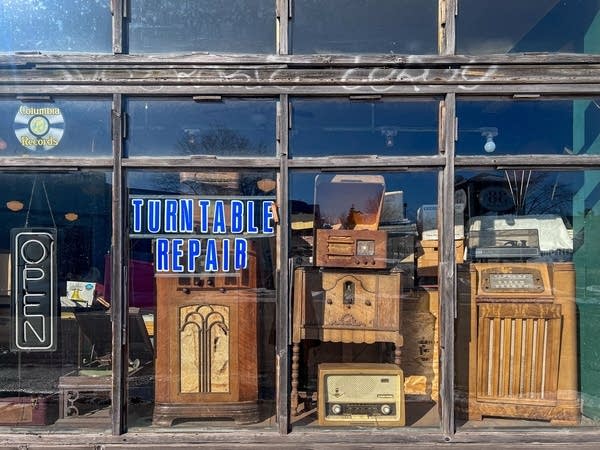 Old radios are lined up in a window display, seen from outside.