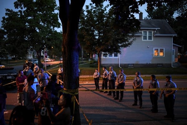 Police form a line in the street as a crowd grows.