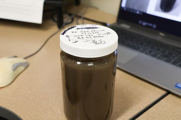 A jar on a desk holds dark brown sediment pollution.