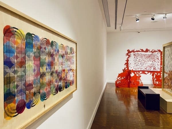 A colorful art piece hangs on a white wall in an art gallery.