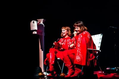 Two women smile and laugh while speaking into microphones onstage