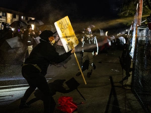 Un manifestant brandit une pancarte alors qu'ils sont aspergés de poivre 