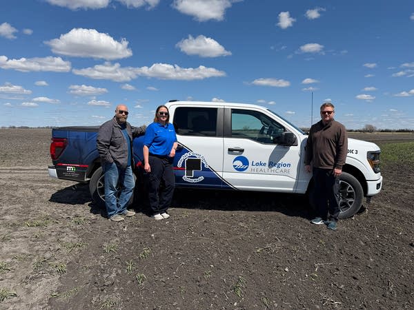 A woman and two men pose next to a white and blue pickup truck.