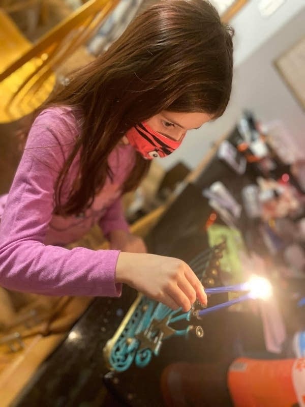 A young girl with a mask lights a candle