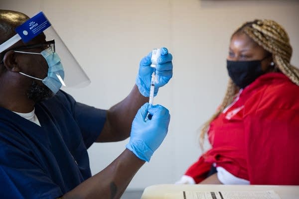 A man pulls a shot into a vial with a woman sitting next to him.