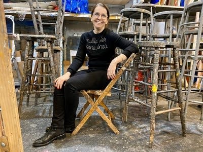 A woman poses next to stacked stools in an art studio.