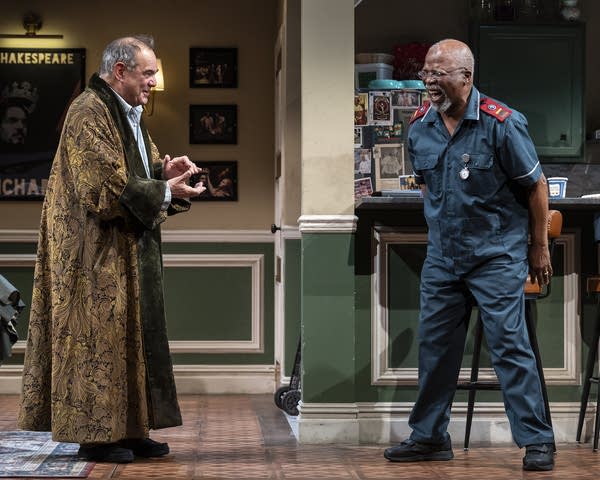 A photo of two actors on set in a play. One wears an ornate robe and the other wears a blue military uniform.