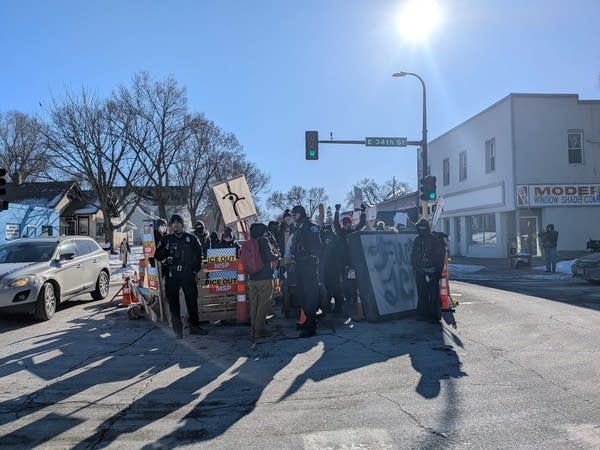 A large group with signs blocks part of a street, forming a blockade for traffic.