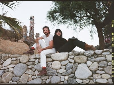 Two people sit on a stone wall for a portrait