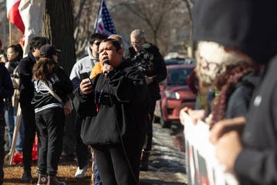 A person speaks into a microphone while surrounded by protesters.