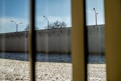 The prison wall is seen from a window across the hall from cells.