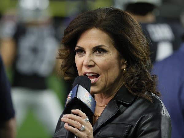 A woman holds a microphone on the sidelines of a football game