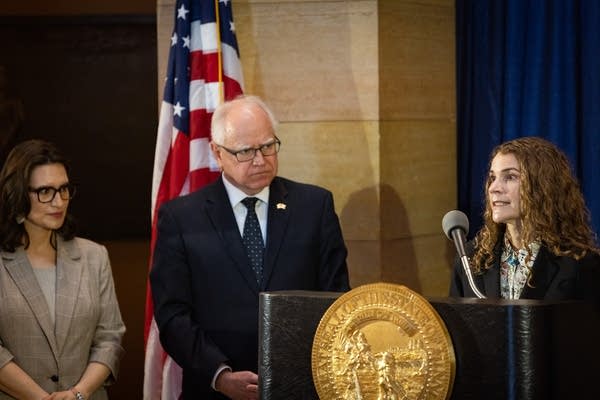 A woman speaks at a podium while the governor and lt. governor listen