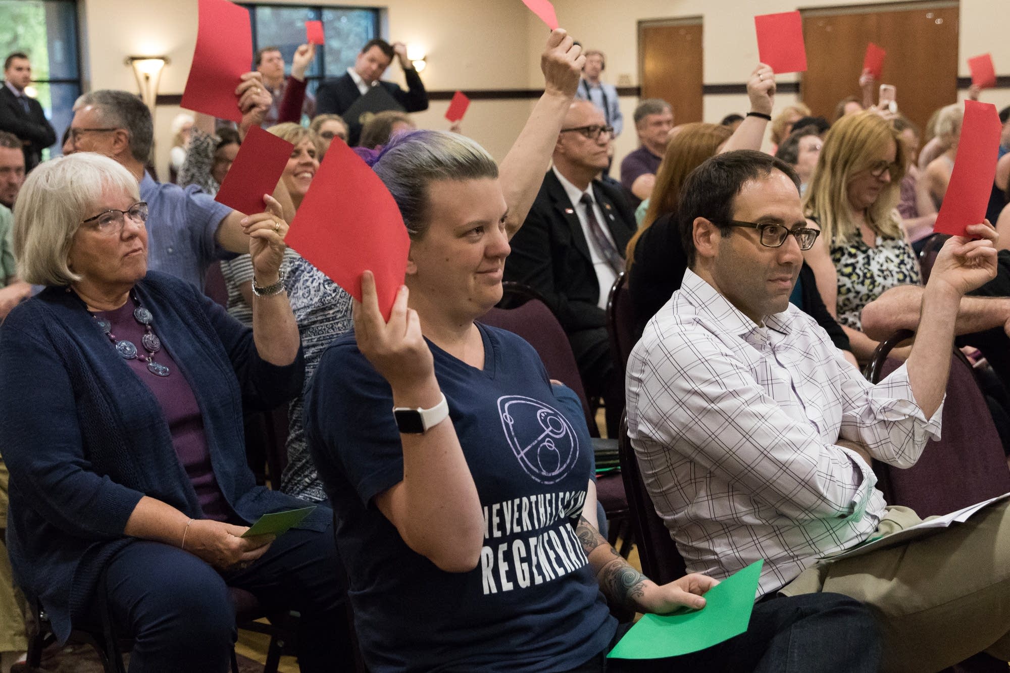 Town hall attendees raise red cards in the air to show they disagree.