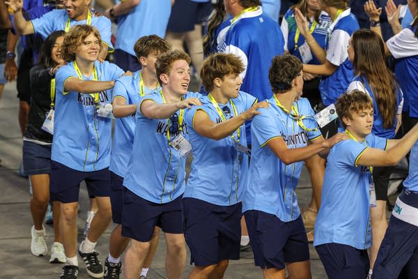 Athletes in light blue shirts form a conga line.
