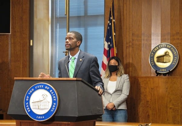 The mayor of St. Paul speaks to the press, a council member stand behind.