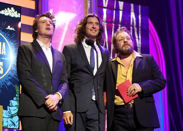 Three musicians speaking together onstage