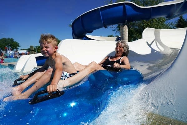 A young boy and a woman go down a water slide on an innertube