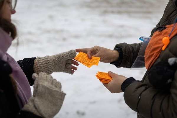 A person hands out bright orange cards
