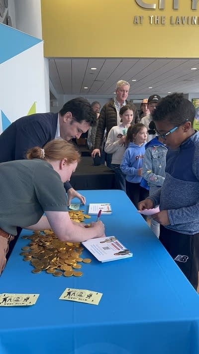 Million Bazillion hosts signing autographs on a table next to a line of young fans