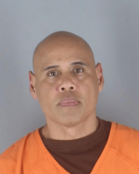 Mugshot of a man in an orange jumpsuit against a gray background.