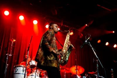 A musician plays saxophone onstage while another plays percussion
